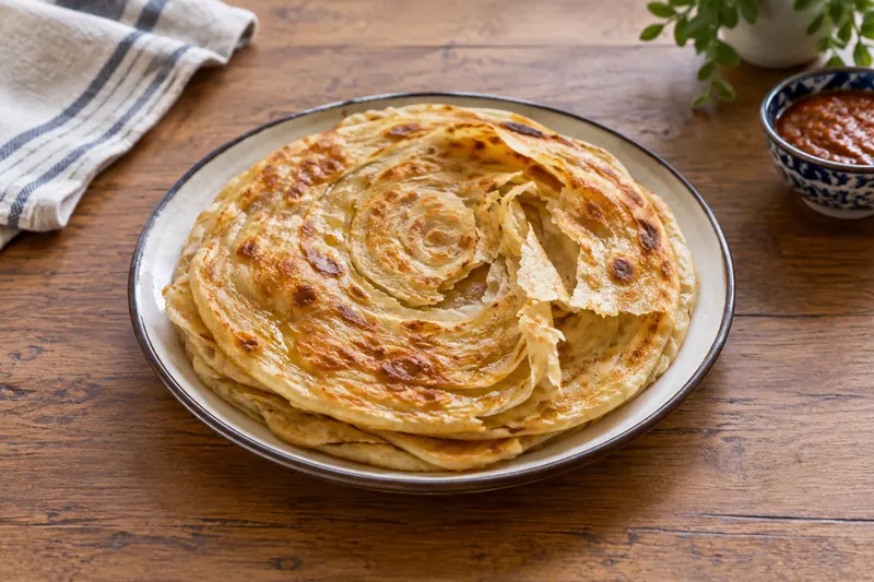 A stack of golden, flaky, layered flatbreads with brown spots, one torn to show layers