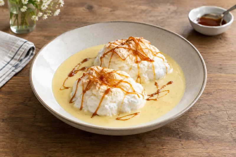 A white meringue island floating in pale vanilla custard with golden caramel threads and toasted almonds