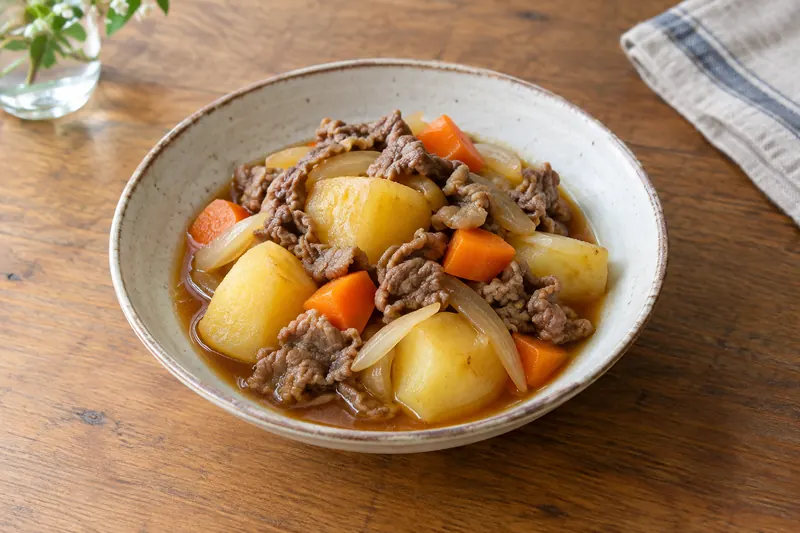 A bowl of simmered beef, potatoes, onion, carrot and glass noodles in a light soy broth