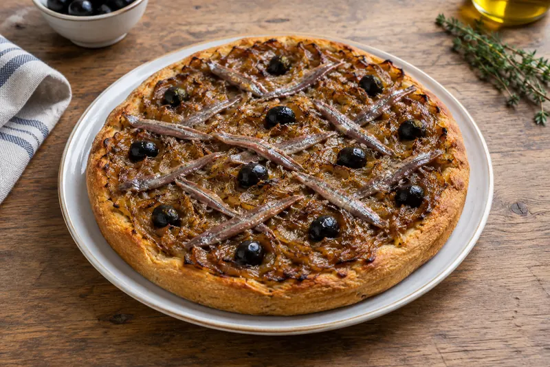 A rectangular tart of soft golden onions with a lattice of anchovies and black olives