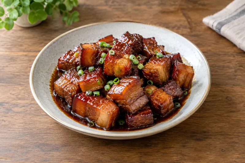 Glossy dark red cubes of braised pork belly with star anise and spring onion