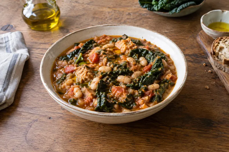 A bowl of very thick bean, cabbage and bread soup with a drizzle of green olive oil